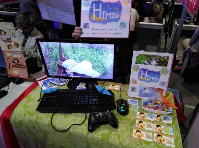 Himig booth with a mini poster, business cards, candies, and a computer playing a trailer of the game.