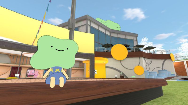 Green blob-faced smiling mascot sitting on a bench. Giant versions of the same face can be seen on top of a building in the background.
